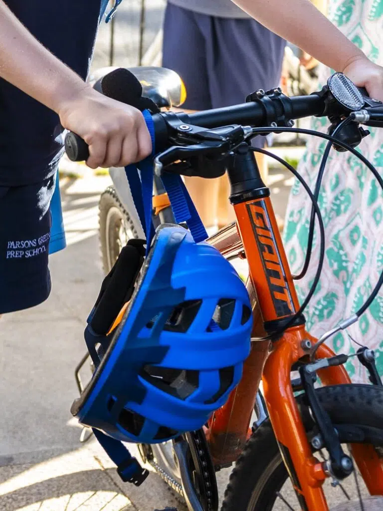 Close-up of an orange bicycle with a blue helmet strapped to the frame and hands gripping the handlebars, outdoors.