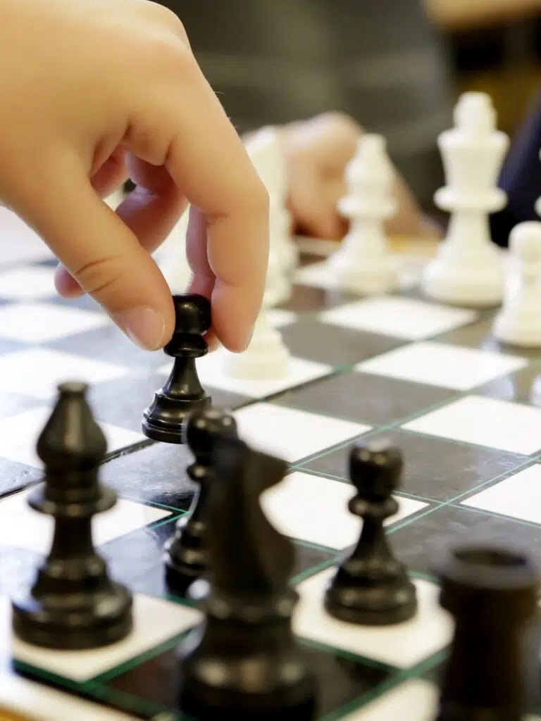Close-up of a hand moving a black chess king on a chessboard, with white pieces visible in the background.