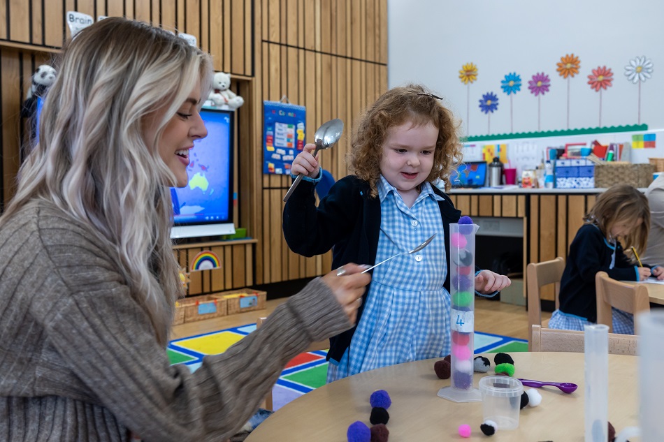 student holding a spoon as the teacher helps out