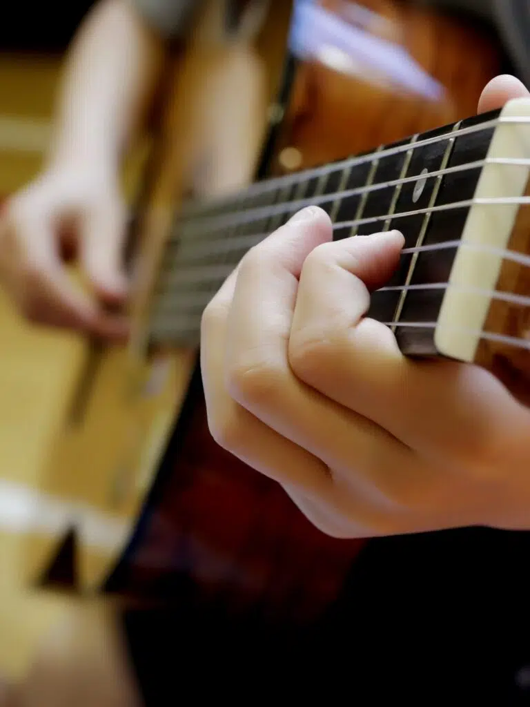 Close-up of a hand pressing guitar strings on the fretboard (left hand) while playing an acoustic guitar.