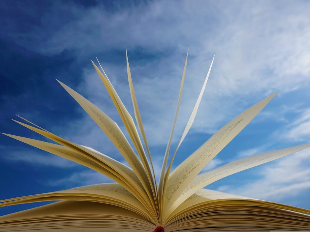 Open book with pages fanned upward, set against a bright blue sky, conveying imagination and learning
