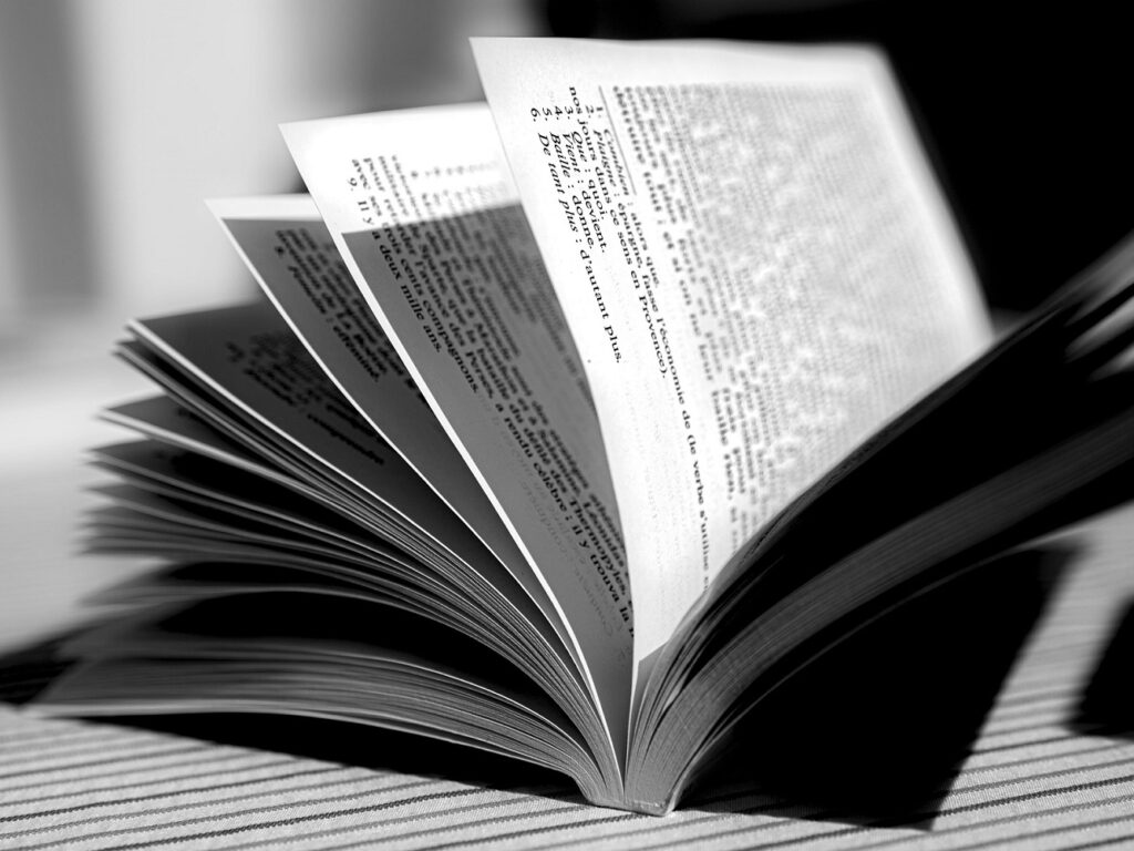 Open book with pages fanned out on a striped surface (black-and-white photo).