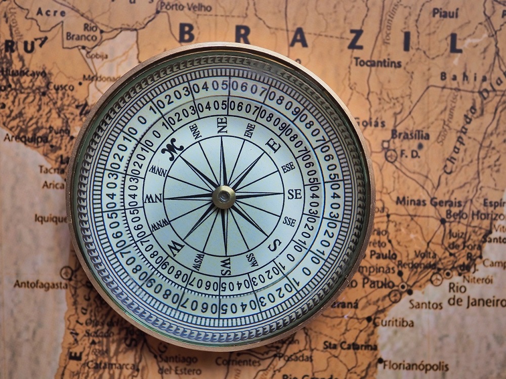 Compass with a blue face showing cardinal directions resting on a vintage map.