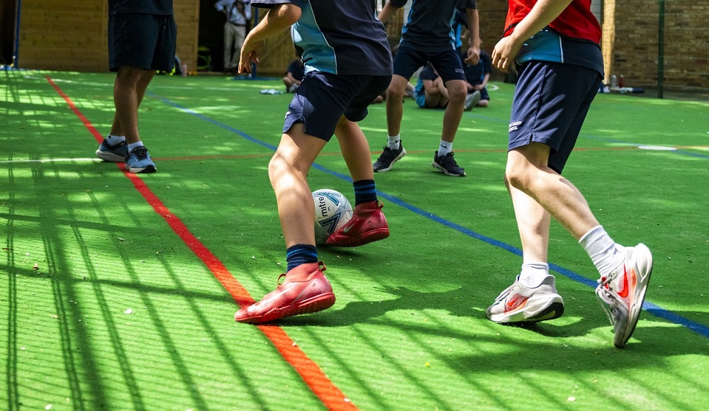 Youth soccer players dribble and contest a ball on a bright green turf surface outdoors.