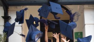 Graduates tossing blue graduation caps into the air outside a building, hands raised in celebration.
