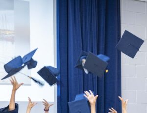 Graduates throwing blue mortarboards into the air at a ceremony on stage.
